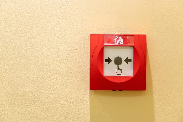 Red manual fire alarm pull station mounted on a yellow wall. Learn how to choose the right fire alarm system for easy activation during emergencies.