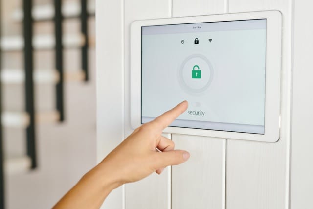 A hand is pointing at a digital display screen showing a lock symbol, representing the management of a security system. Regular access control systems maintenance is key to ensuring your system functions properly.