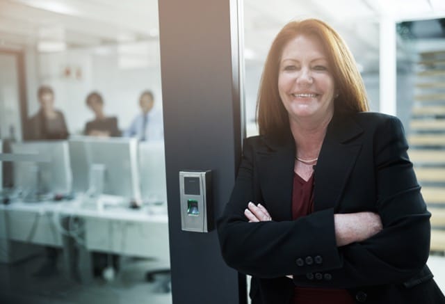 A businesswoman confidently stands by a door with a biometric access control system. Learn how to choose the right access control system for your office security.