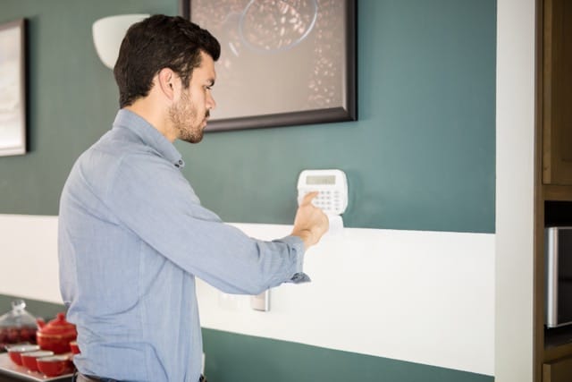 Young man in front of a keypad typing his password to activate his home Intruder Alarm alarm system