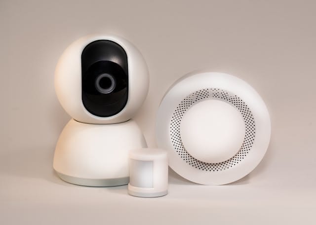 Intruder alarm system features showing a security camera, motion sensor, and another sensor device with perforated design.