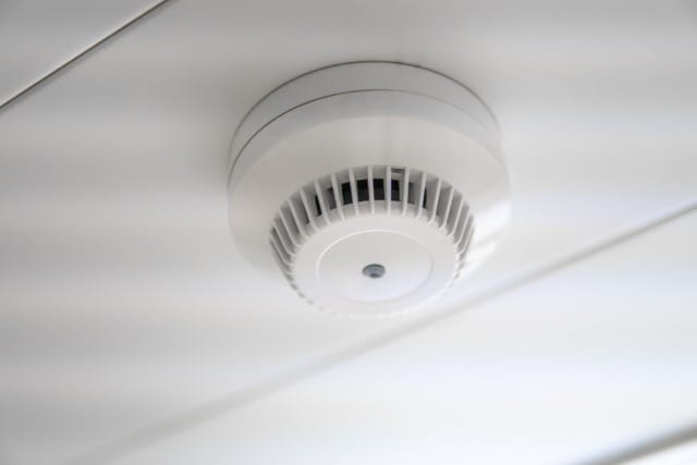 Ceiling-mounted white smoke detector with vents. This is an example of a fire alarm system to consider when choosing the best for your space.