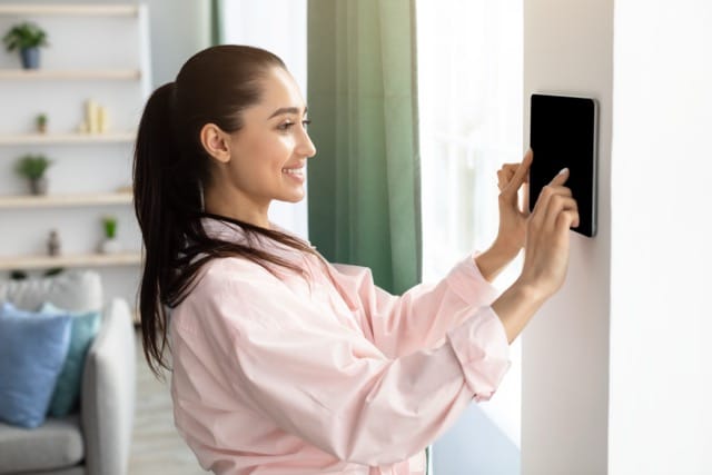 A woman is interacting with a smart wall control panel at home, managing her security system. Proper access control systems maintenance ensures that systems like these remain effective in protecting your home.