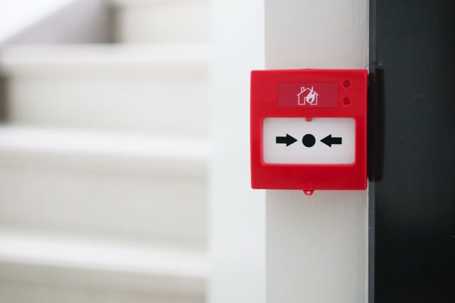 Red fire alarm button on the wall represents the fire alarm, which is an important thing in security systems.