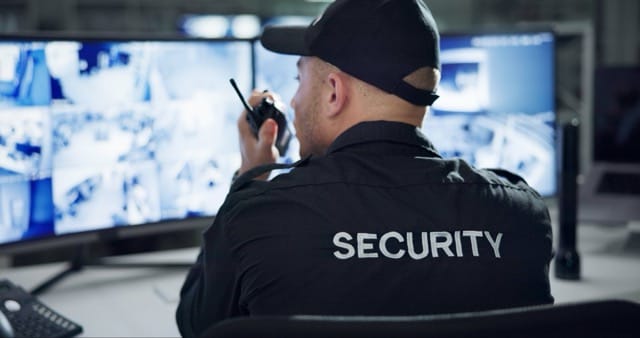 A security guard uses a walkie-talkie while monitoring CCTV footage. This image shows the vital Security Guard Services Benefits of surveillance and rapid response in ensuring safety and security